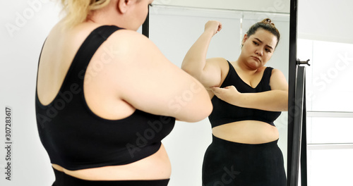 Chubby woman standing and looking at her arm in a mirror.