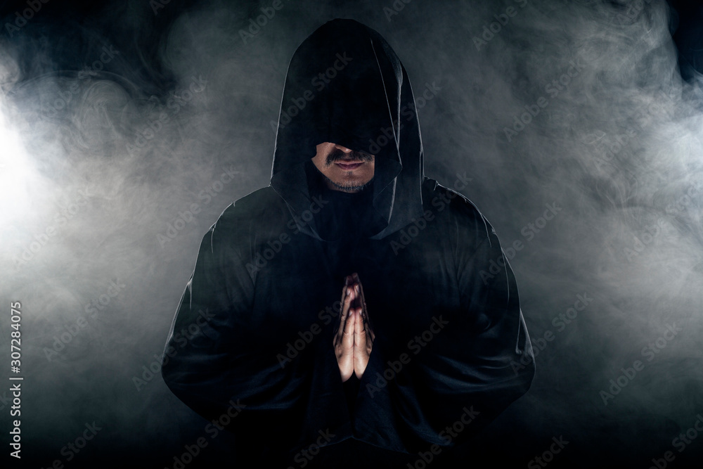 Foto de Man dressed in a dark robe looking like a cult leader on a smoky or  foggy background. He looks like a creepy evil villain do Stock