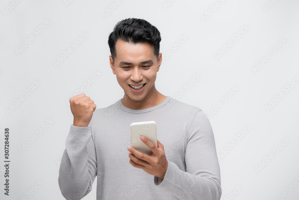 Happy excited Asian man looking at his smartphone and raising his arm up to celebrate success Happy excited Asian man looking at his smartphone and raising his arm up to celebrate success