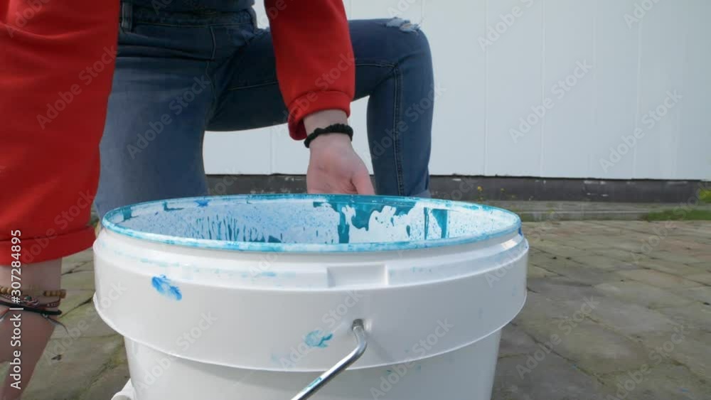 Close up slow motion of a girls hand is opening a paint bucket wih blue
