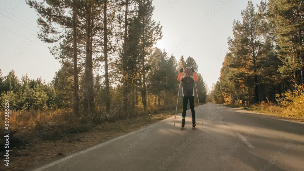 Training an athlete on the roller skaters. Biathlon ride on the roller skis with ski poles, in the helmet. Autumn workout. Roller sport. Adult man riding on skates. Training an athlete on the roller skaters. Biathlon ride on the roller skis with ski poles, in the helmet. Autumn workout. Roller sport. Adult man riding on skates.