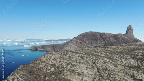Slow ascending drone view of the rocky terrain of Kullorsuaq, Greenland, coasting the deep blue arctic sea, showing high details of the ground surface and icebergs that float in the Baffin sea