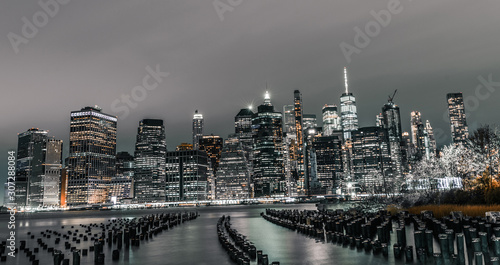 Old wooden pylons jutting out of water long exposure photograph with lower Manhattan in view at night