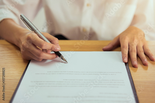 Woman signing document and hand holding pen putting signature at paper, order to authorize their rights.
