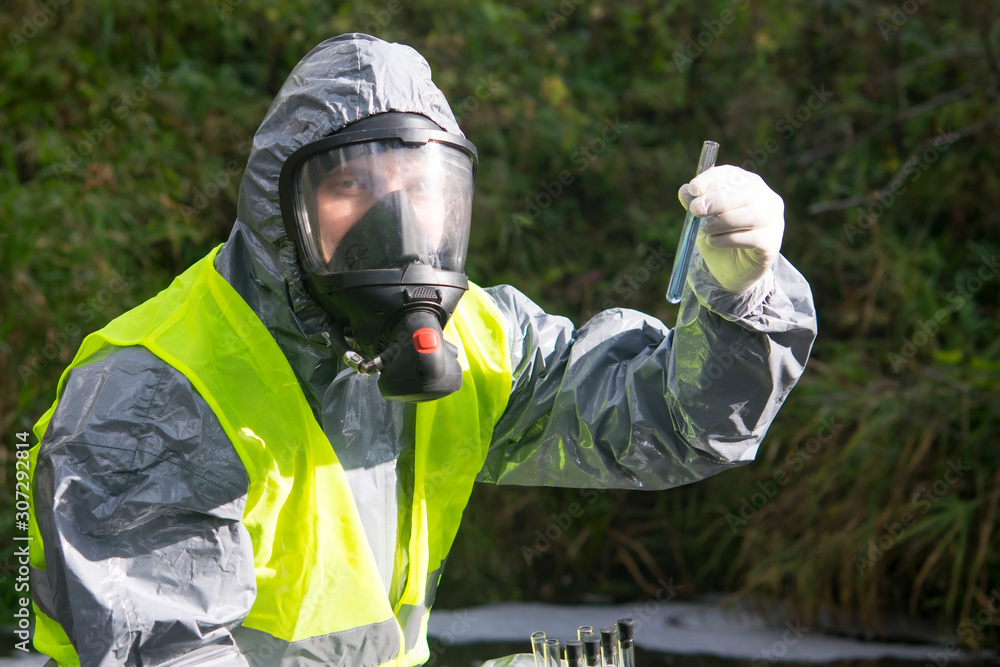 specialist in a gray protective suit and mask, takes a sample of liquid in test tubes from the river, close-up specialist in a gray protective suit and mask, takes a sample of liquid in test tubes from the river, close-up