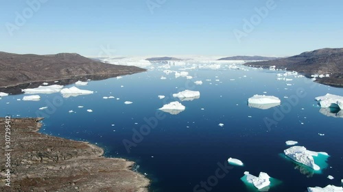 Aerial drone view of the arctic scenery of the area of Kullorsuaq, Greenland, with the deep blue and turquoise sea of Baffin, highly detailed natural rocky terrain and white icebergs floating