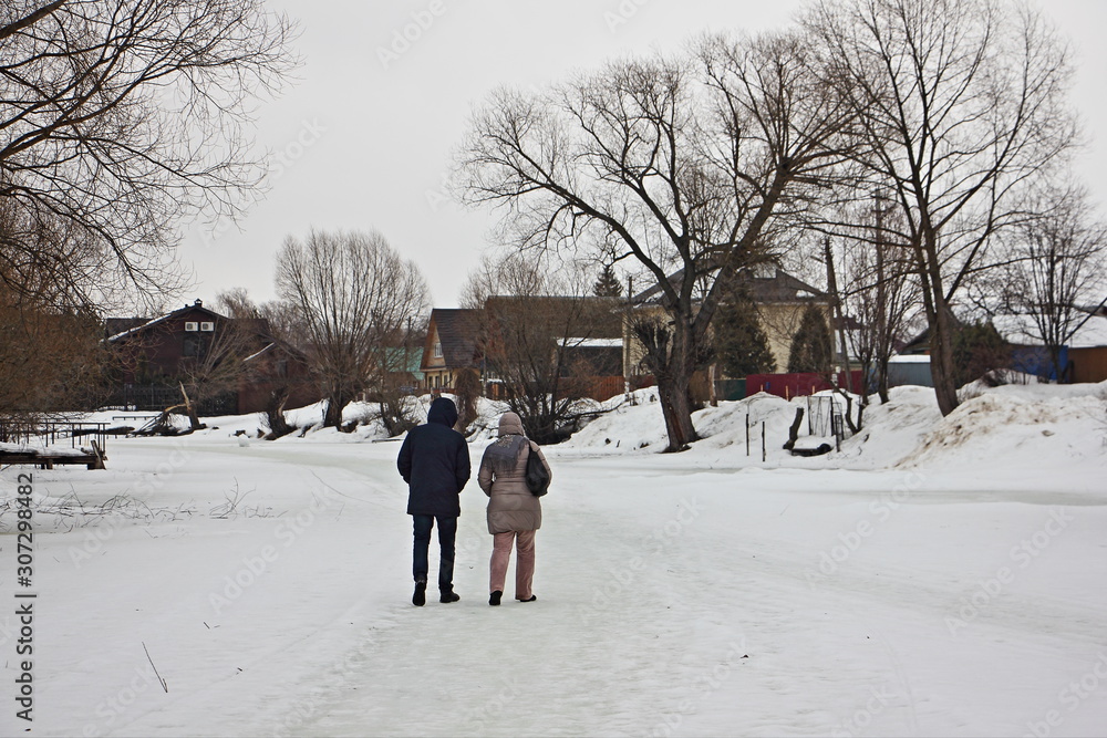 A couple of tourists a man and a woman walk along the ice of the frozen snow covered winter river