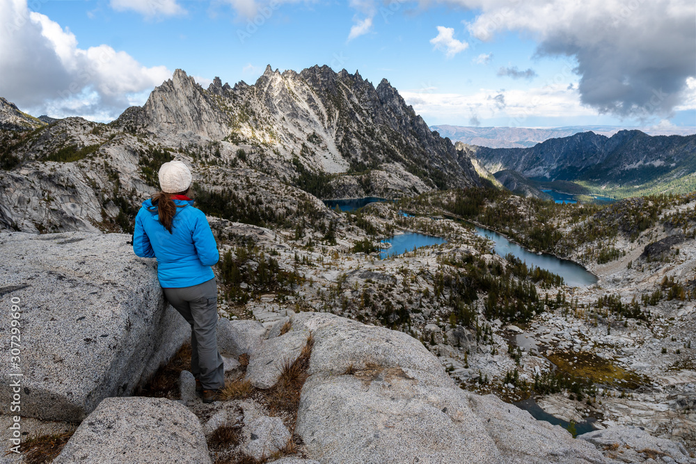 Female hiker enjoying an epic view of towering peaks and alpine lakes