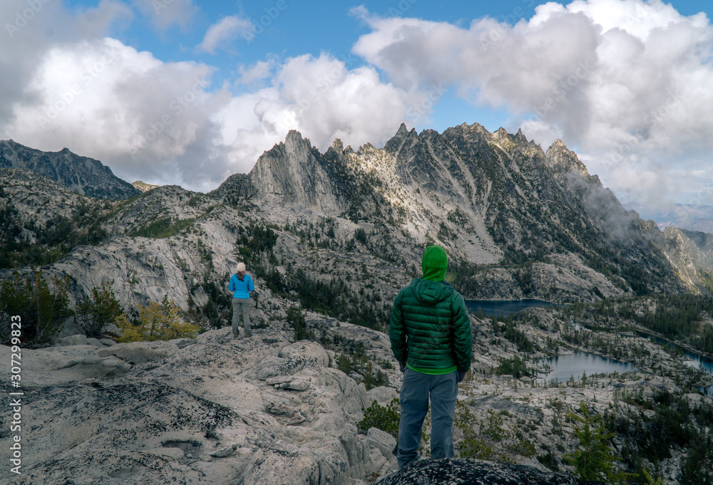 Two adventurers look across stunning alpine vista with blue lakes and rugged peaks