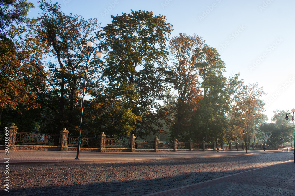 Sights and views of Grodno. Belarus. Fragment of the streets of the old city in the morning sun. The road is covered with old tiles. Trees of the park.