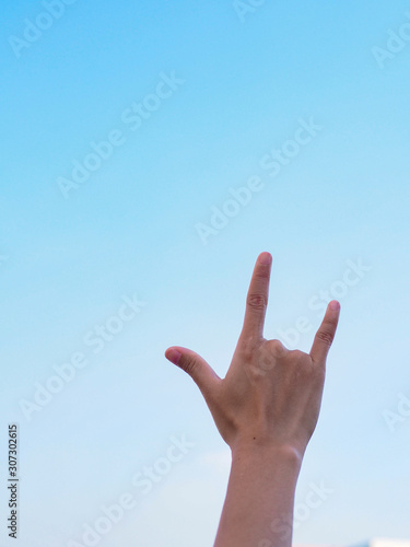 Human hand show love sign on blue sky as a background.