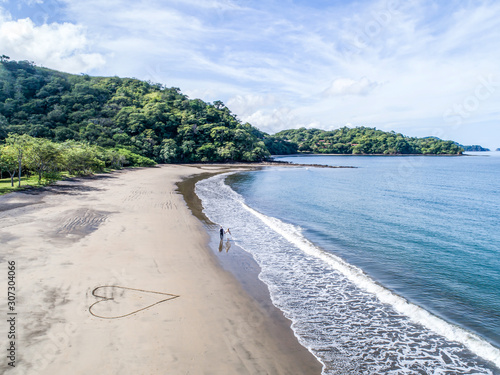 Aerial shot of wedding dress couple on the tropical beach Playa Arenillas in Costa Rica with a heart drawn into Sand