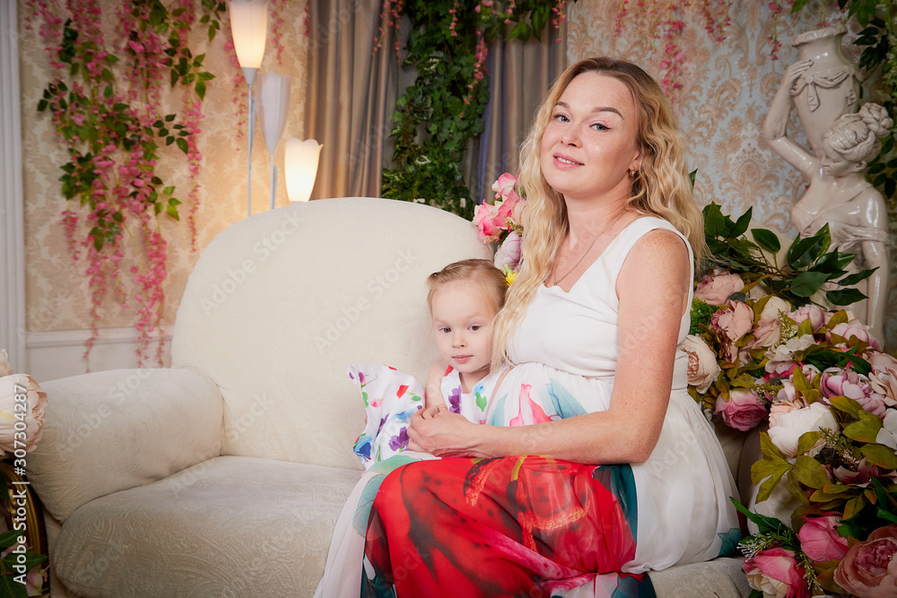Happy mother and daughter in bright summer dresses having hugs and smiles. Happy mother's Day in living room with flowers Happy mother and daughter in bright summer dresses having hugs and smiles. Happy mother's Day in living room with flowers