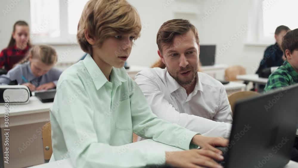 Education in the modern school, children use laptops, teacher communicates with the student and discusses the performance of the test work. Education in the modern school, children use laptops, teacher communicates with the student and discusses the performance of the test work.