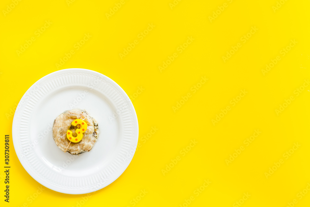 Cat's birthday concept. Pet feed with festive candle in shape of three on yellow background top-down copy space Cat's birthday concept. Pet feed with festive candle in shape of three on yellow background top-down copy space