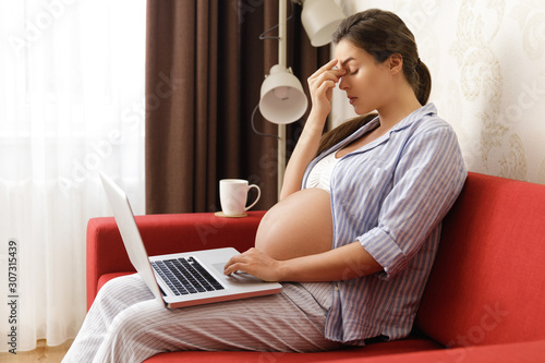 Tired pregnant woman sitting with a laptop computer