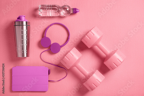 Dumbbells, headphones and protein shaker on the fitness mat