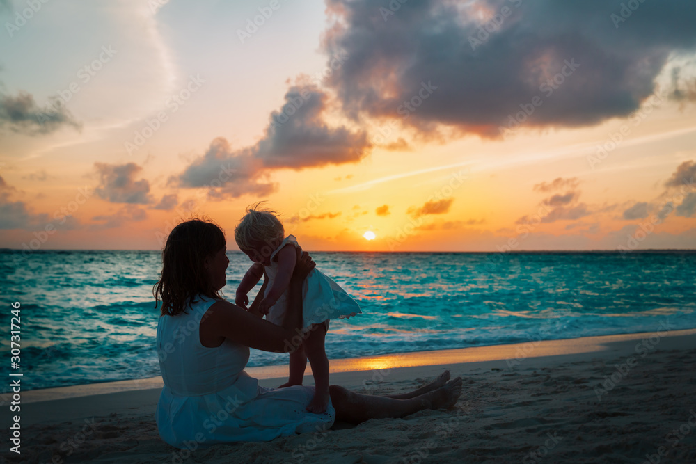 happy mother and little daughter play at sunset beach