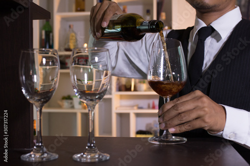 Waiter pouring wine into glasses at the bar.