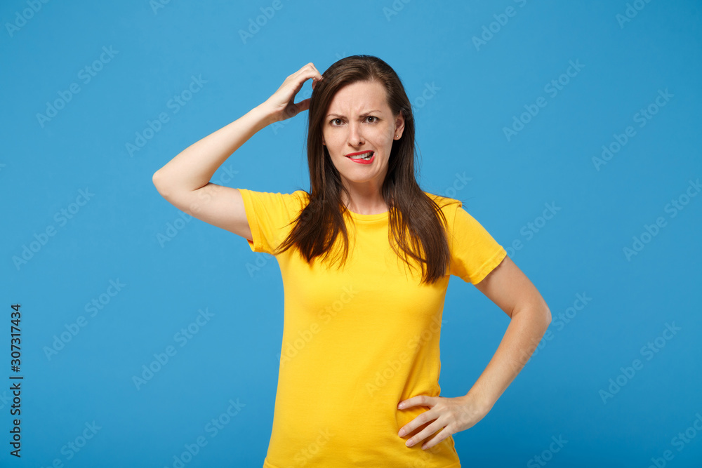 Preoccupied young brunette woman girl in yellow t-shirt posing isolated on bright blue wall background studio portrait. People lifestyle concept. Mock up copy space. Putting hand on head, biting lips. Preoccupied young brunette woman girl in yellow t-shirt posing isolated on bright blue wall background studio portrait. People lifestyle concept. Mock up copy space. Putting hand on head, biting lips.