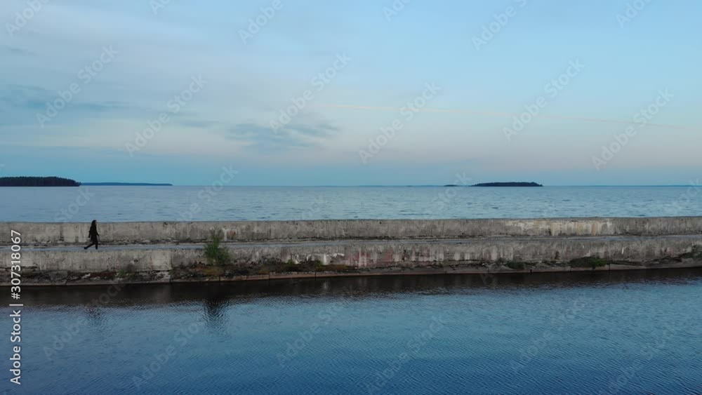 A lonely, brooding man in black clothes walks along an old stone breakwater, against a background of blue sky and sea. Aerial view of beautiful landscape A lonely, brooding man in black clothes walks along an old stone breakwater, against a background of blue sky and sea. Aerial view of beautiful landscape