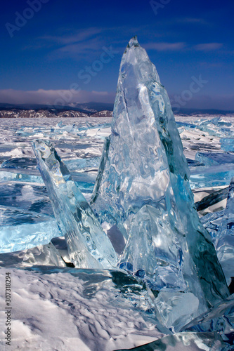A large broken transparent piece of ice stands frozen vertically on Lake Baikal. A lot of broken ice around. Beautiful blue and green color of ice. Vertical.