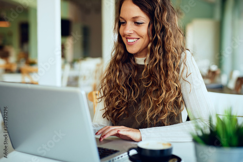 Attractive young curly brunette enjoying her coffee/tea and working on tablet