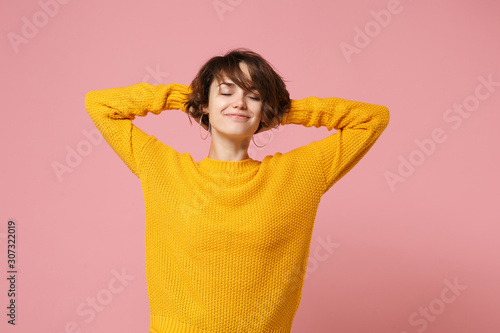 Relaxed young brunette woman girl in yellow sweater posing isolated on pastel pink wall background, studio portrait. People lifestyle concept. Mock up copy space. Sleeping with hands behind head. © ViDi Studio