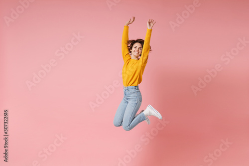 Cheerful young brunette woman girl in yellow sweater posing isolated on pastel pink background in studio. People lifestyle concept. Mock up copy space. Having fun fooling around rising hands, jumping.