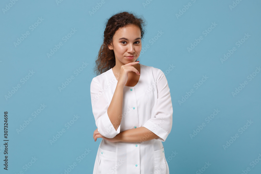 Beautiful african american doctor woman isolated on blue background. Female doctor in white medical gown put hand prop up on chin. Healthcare personnel health medicine concept. Mock up copy space. Beautiful african american doctor woman isolated on blue background. Female doctor in white medical gown put hand prop up on chin. Healthcare personnel health medicine concept. Mock up copy space.