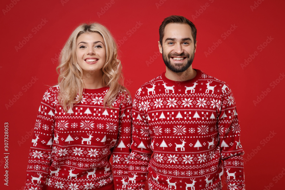 Merry young couple guy girl in Christmas knitted sweaters posing together isolated on bright red background studio portrait. Happy New Year 2020 celebration holiday party concept. Mock up copy space.