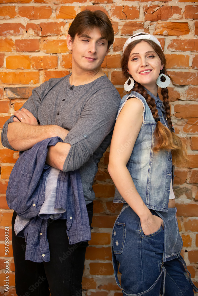 Vertical guy and girl are standing against a brick wall. Young couple in jeans clothes