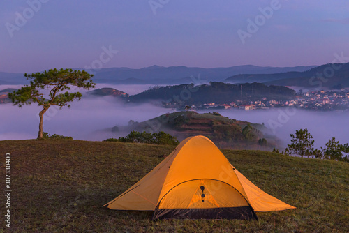 Glowing tent on the hill with misty valley landscape