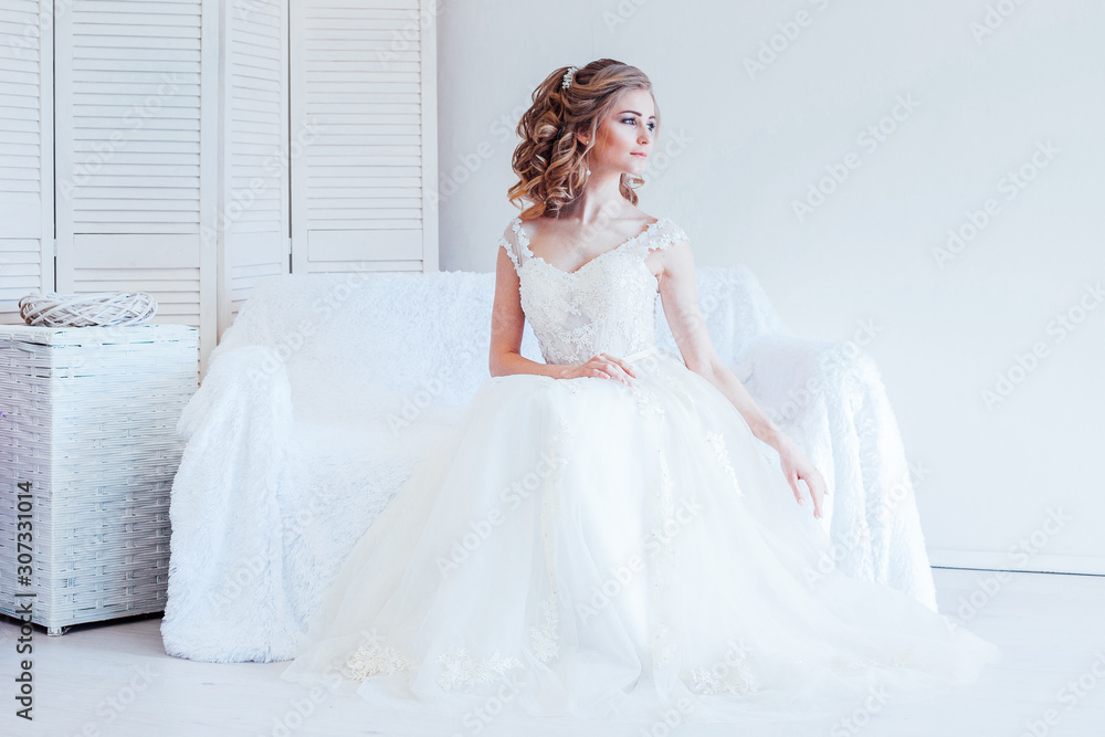 beautiful bride sitting on a white couch in wedding dress