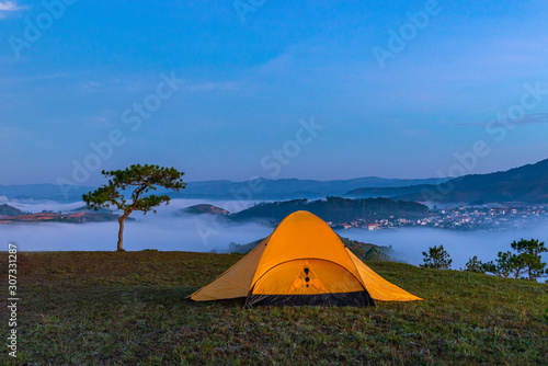 Yellow tent camping on hill under misty weather at dawn 