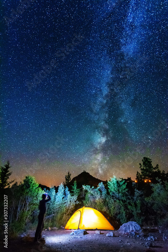 Fototapeta Naklejka Na Ścianę i Meble -  Vertical landscape images with a night starry sky and a milky way against the backdrop of a yellow tourist tent, which is highlighted from the inside.