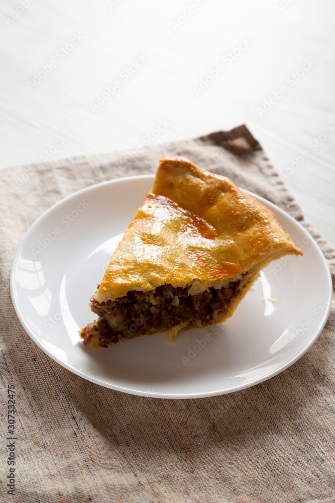 Slice of Homemade Canadian Tourtiere Meat Pie on a white plate , side view. Copy space. Slice of Homemade Canadian Tourtiere Meat Pie on a white plate , side view. Copy space.