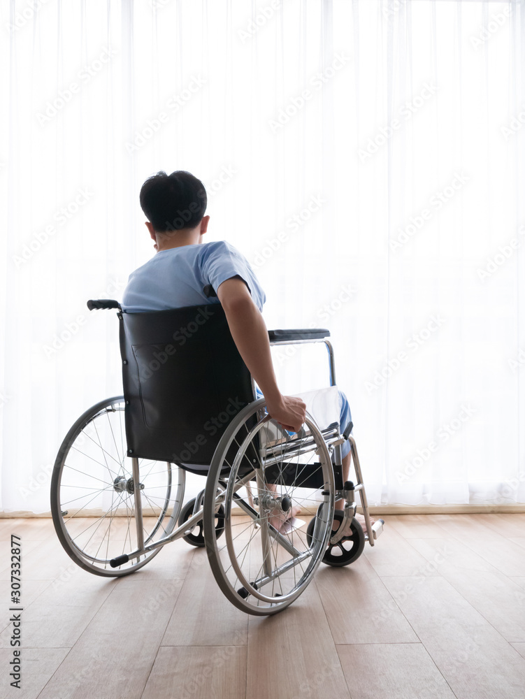 Asian patient disability man sitting alone on wheel chair vehicle near big window with white curtain in a clean room at clinic waiting for professional doctor and nurse take care of physical therapy Asian patient disability man sitting alone on wheel chair vehicle near big window with white curtain in a clean room at clinic waiting for professional doctor and nurse take care of physical therapy