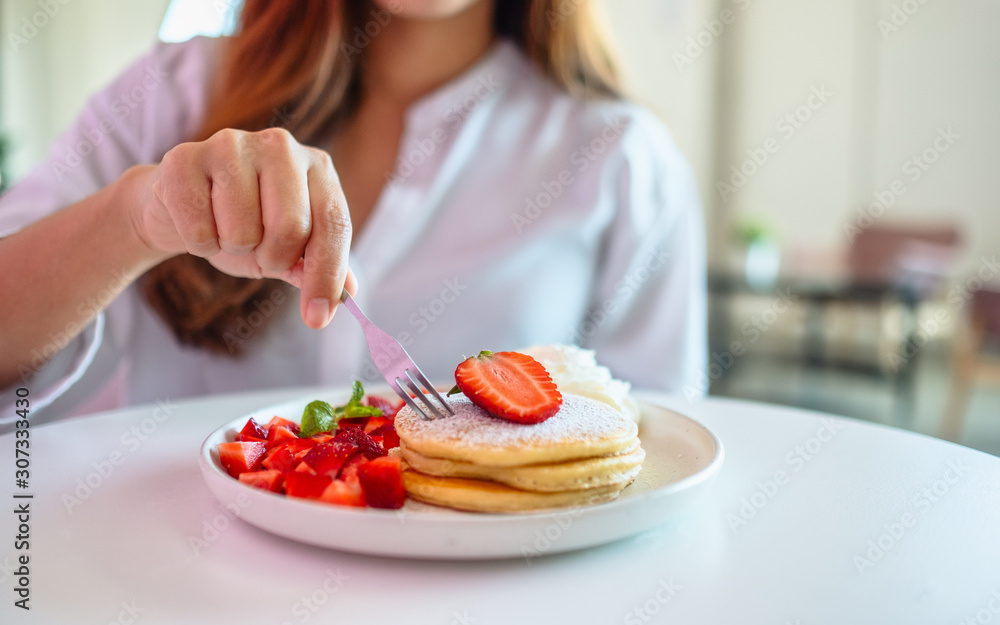 A woman holding and eating pancakes with strawberries and whipped cream by fork