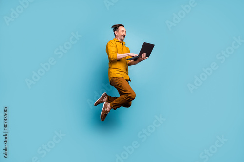 Full body photo of cheerful excited man jump use computer search online social media black friday sales discounts wear casual style clothes isolated over blue color background