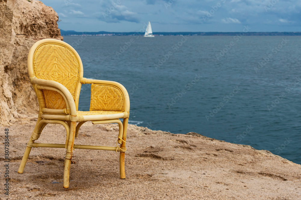wicker chair on the stone beach against the blue sea and white yacht