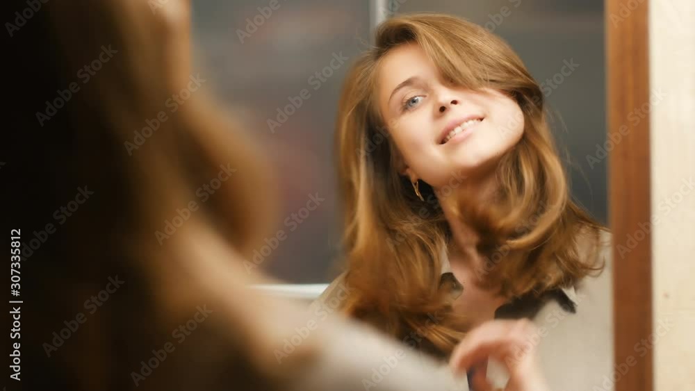 reflection of a cute girl preens herself in front of a mirror at home,beautiful young woman straightens her hair, concept female beauty and fashion reflection of a cute girl preens herself in front of a mirror at home,beautiful young woman straightens her hair, concept female beauty and fashion