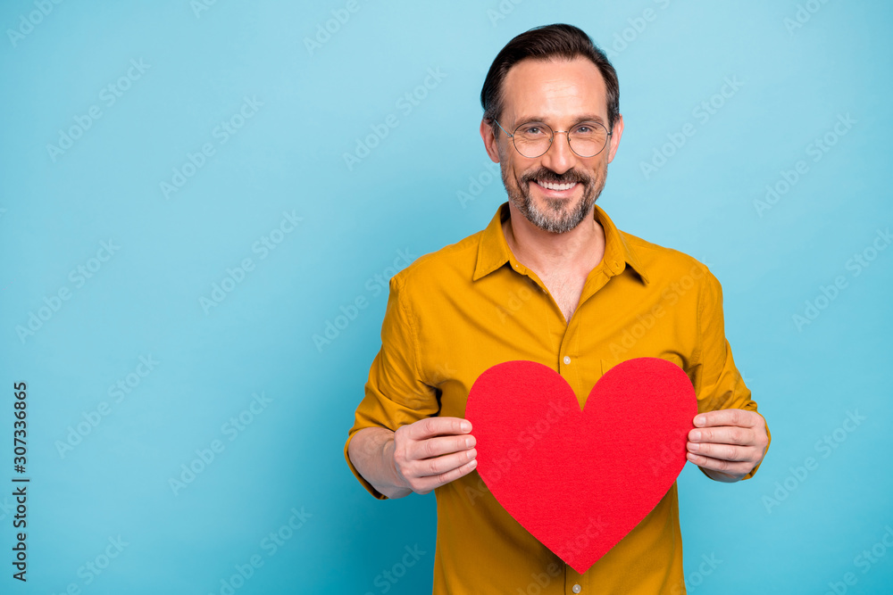 Portrait of positive cheerful man hold red paper card heart present for his wife on 14-february dating party celebration wear stylish shirt isolated over blue color background Portrait of positive cheerful man hold red paper card heart present for his wife on 14-february dating party celebration wear stylish shirt isolated over blue color background