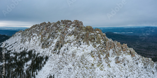 Panorama of Ural national park Taganay in winter cloudy day; snowy slopes of Otkliknoy greben mountain, steep rocky gradient; sharp peaks of ridge with steep cliffs for climbing; aerial view; Russia photo