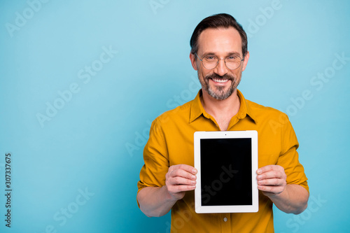 Portrait of cheerful man confident cool promoter hold tablet display gadget recommend adverts promotion wear yellow shirt isolated over blue color background