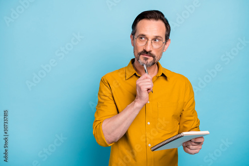 Portrait of serious focused man write essay in his copy book think thoughts contemplate wear modern clothes isolated over blue color background photo