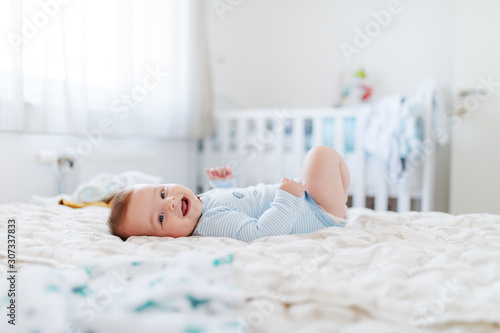 Wallpaper Mural Side view of adorable chubby six months old baby boy lying on bed, smiling and looking at camera. Bedroom interior. Happy childhood concept. Torontodigital.ca