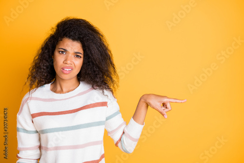 Closeup photo portrait of unhappy sad upset expressing disgust girl showing pointing finger to copy space isolated bright color background