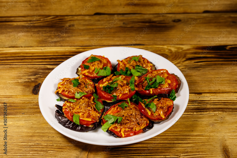 Baked eggplants with tomatoes and cheese on wooden table Baked eggplants with tomatoes and cheese on wooden table