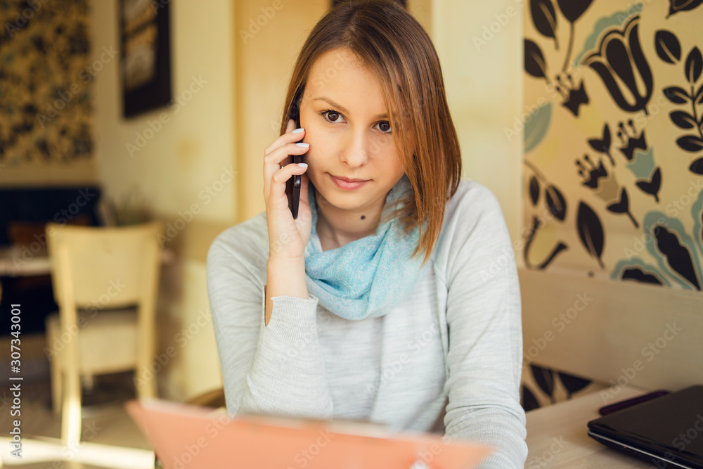 Portrait of beautiful young woman sitting by the table at cafe talking making a call using smart mobile phone Portrait of beautiful young woman sitting by the table at cafe talking making a call using smart mobile phone